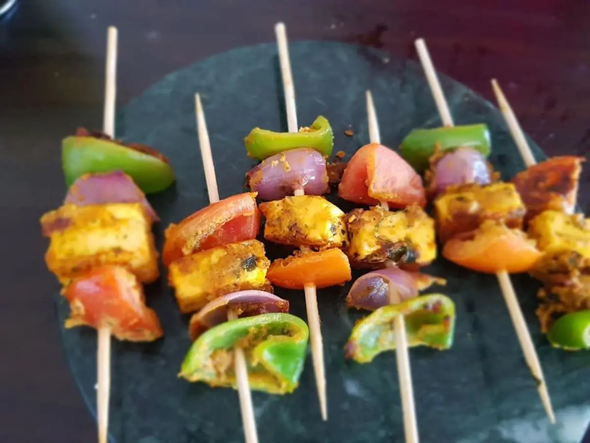 Brochetas de tikka con cubos de queso o tofu, pimiento verde, tomate y cebolla morada sobre pizarra