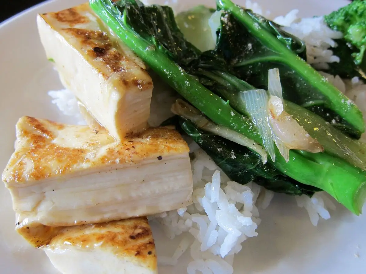 Bloques de tofu ligeramente dorados con verdura china de hoja salteada sobre arroz blanco