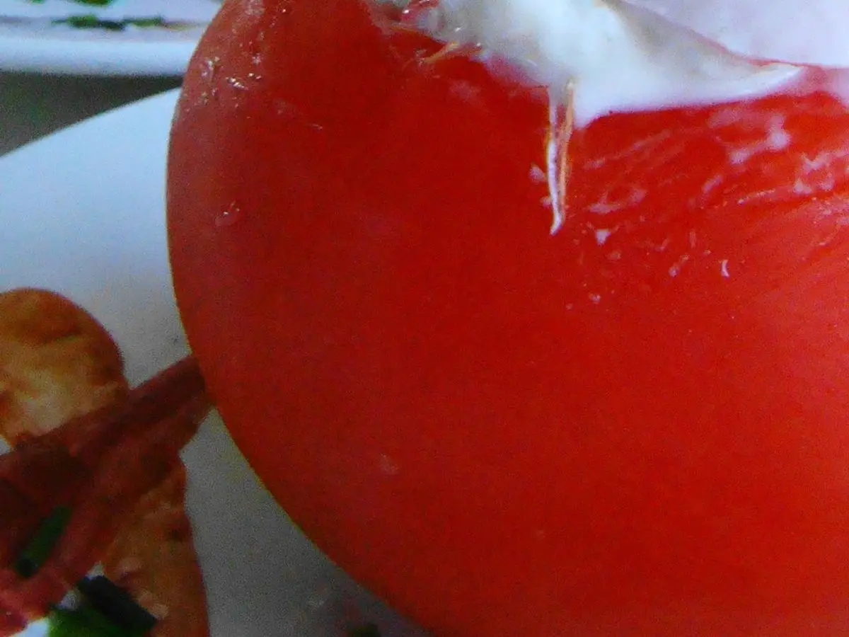 Tomate fresco relleno de una ensalada cremosa blanca con cebollino picado por encima