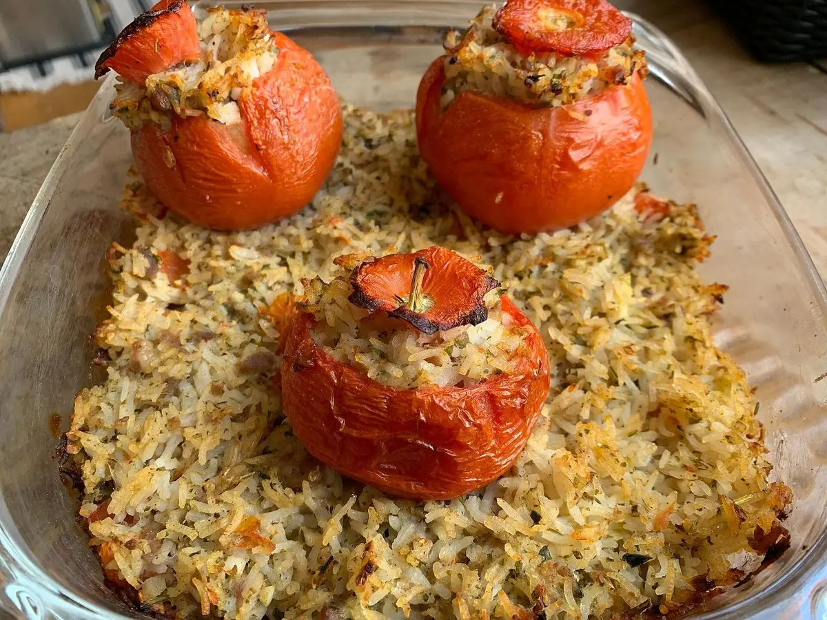 Tres tomates rellenos al horno sobre una cama de arroz en una fuente de cristal