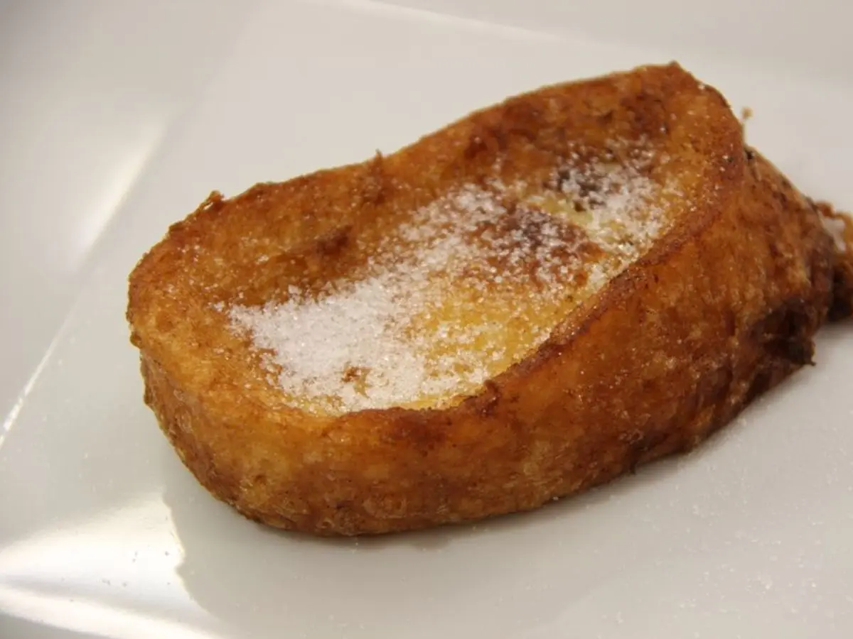 Torrija dorada espolvoreada de azúcar sobre un plato blanco
