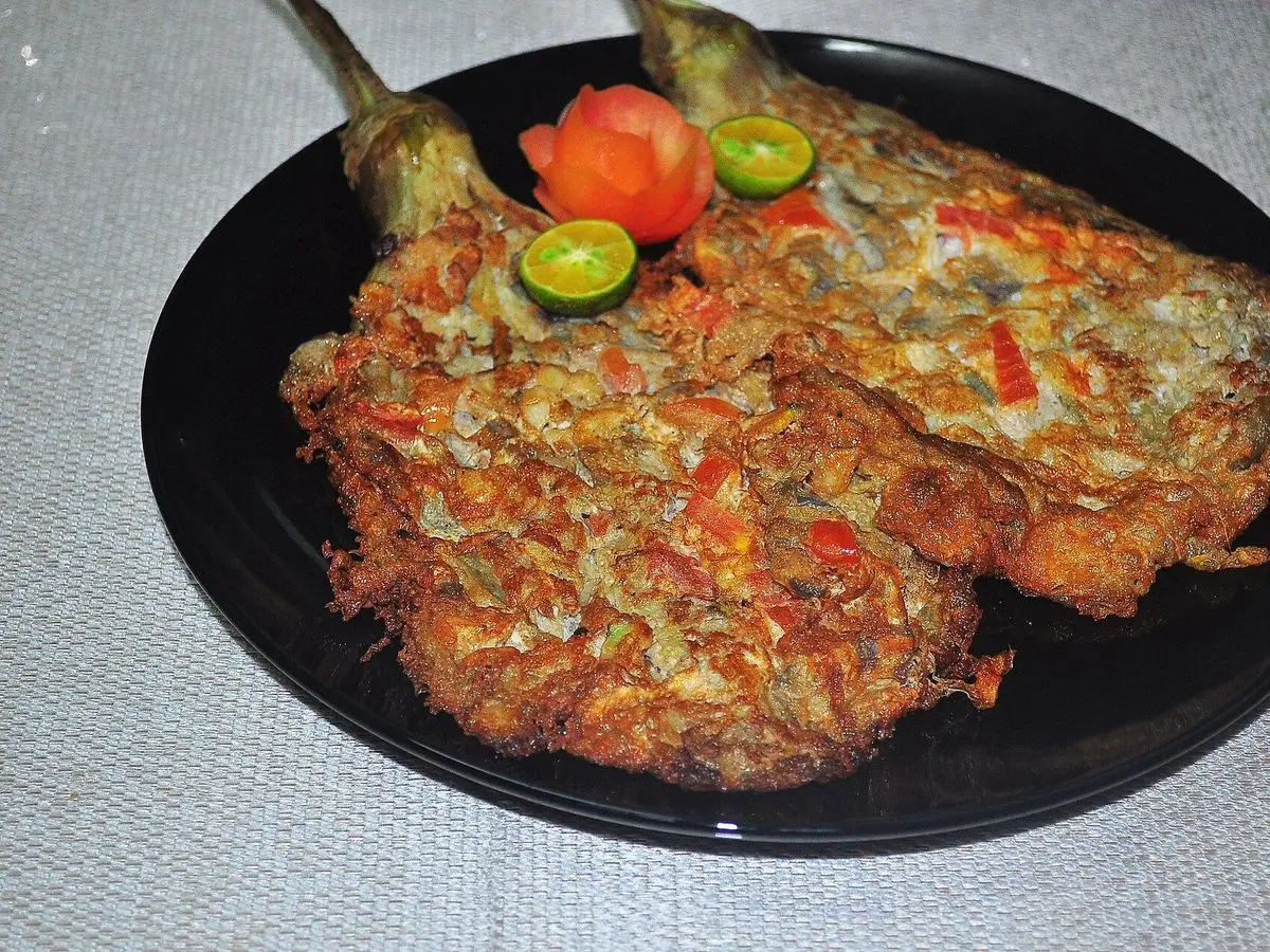 Dos berenjenas asadas rebozadas en huevo con tomate y lima en un plato negro