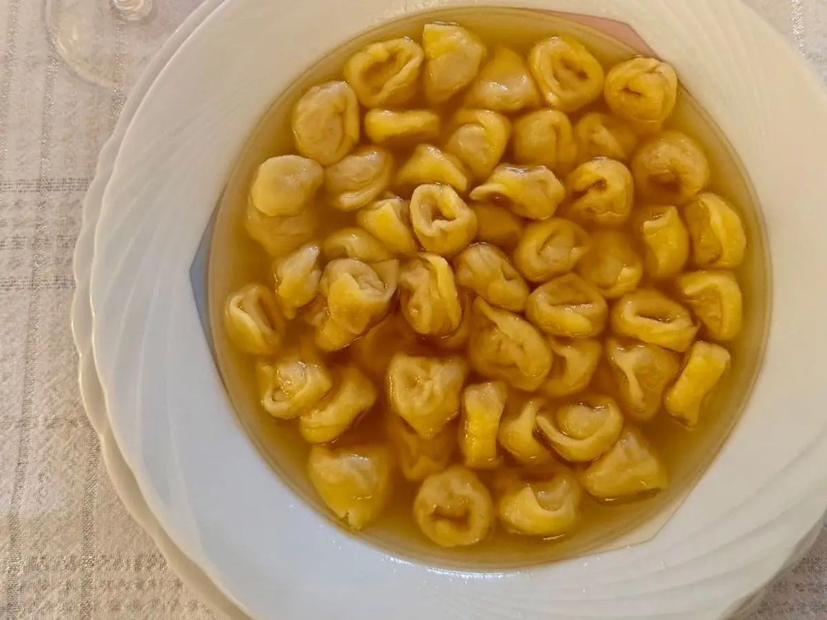 Plato de tortellini en caldo dorado servido en un plato hondo blanco