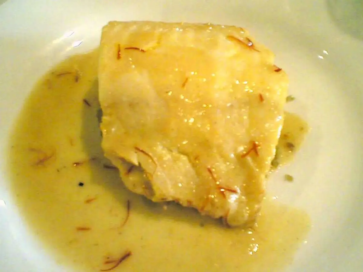 Trozo de eglefino ahumado cocinado en salsa cremosa dorada con hebras de azafrán sobre un plato blanco