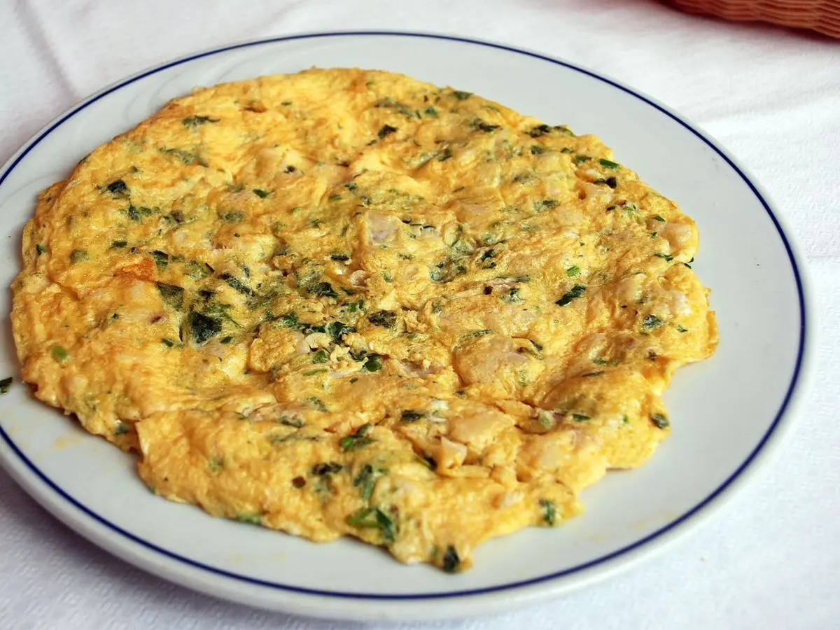 Tortilla de bacalao jugosa con perejil servida en un plato blanco con borde azul