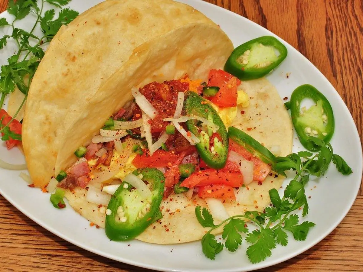 Taco de huevo con pimientos rojos y rodajas de jalapeño verde sobre un plato blanco
