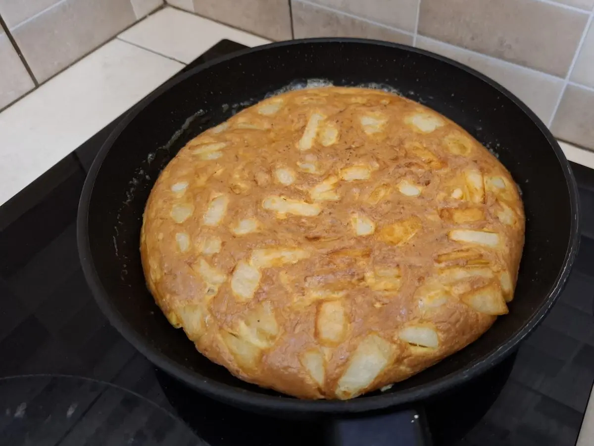 Tortilla gruesa y dorada con trozos de verdura dentro de una sartén negra sobre la placa