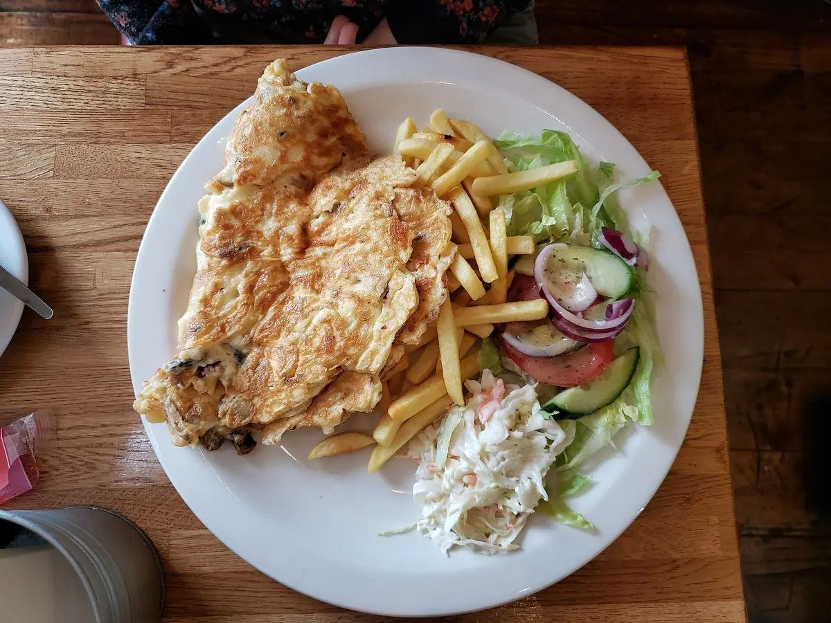 Tortilla de champiñones en un plato blanco con ensalada de tomate, pepino y patatas fritas