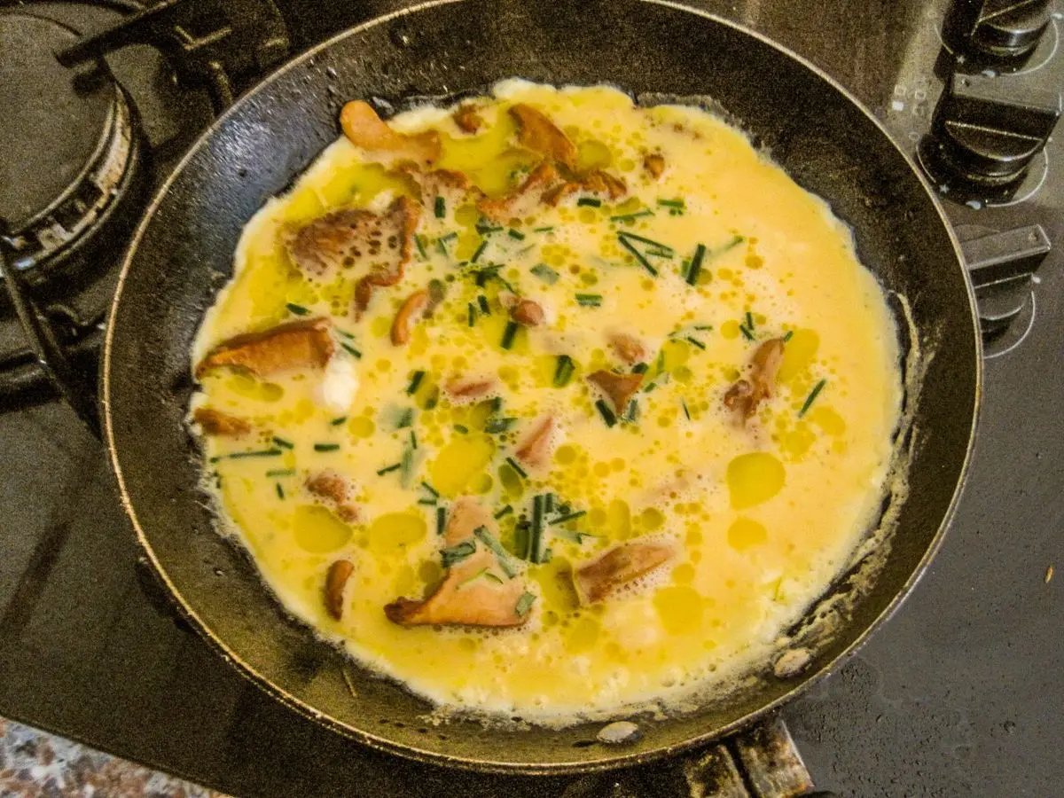 Tortilla de huevo con setas y cebollino cocinándose en una sartén negra