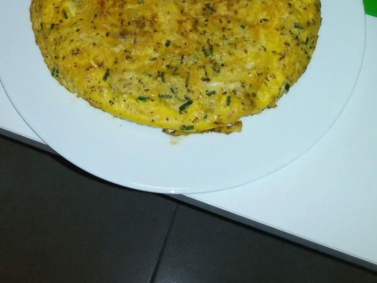 Tortilla redonda dorada de espaguetis y hierbas sobre un plato blanco