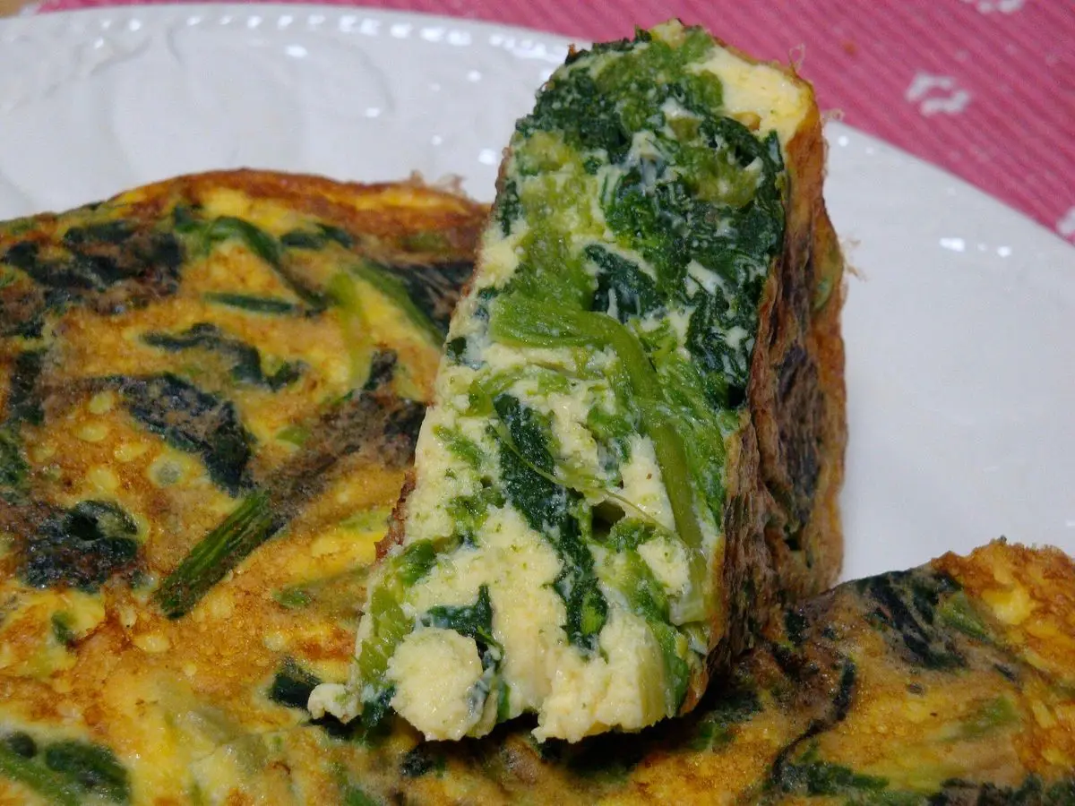 Tortilla cuajada con espinacas cortada en porciones sobre un plato blanco