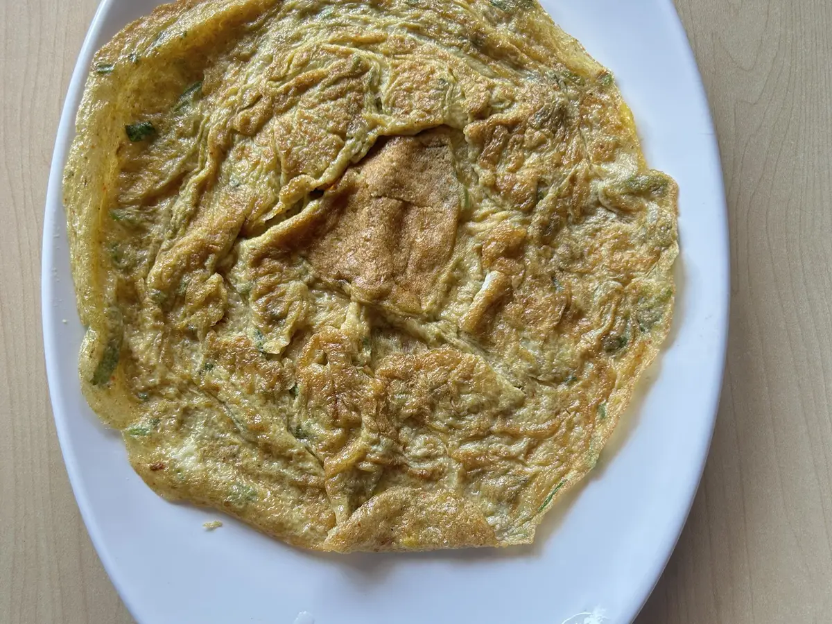 Tortilla francesa dorada con hierbas sobre una fuente ovalada blanca