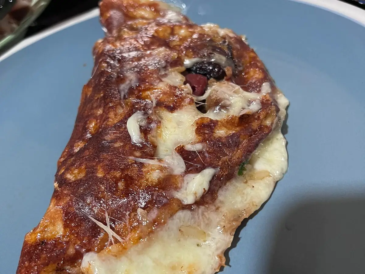 Tortilla doblada y muy dorada con queso fundido asomando sobre un plato azul claro