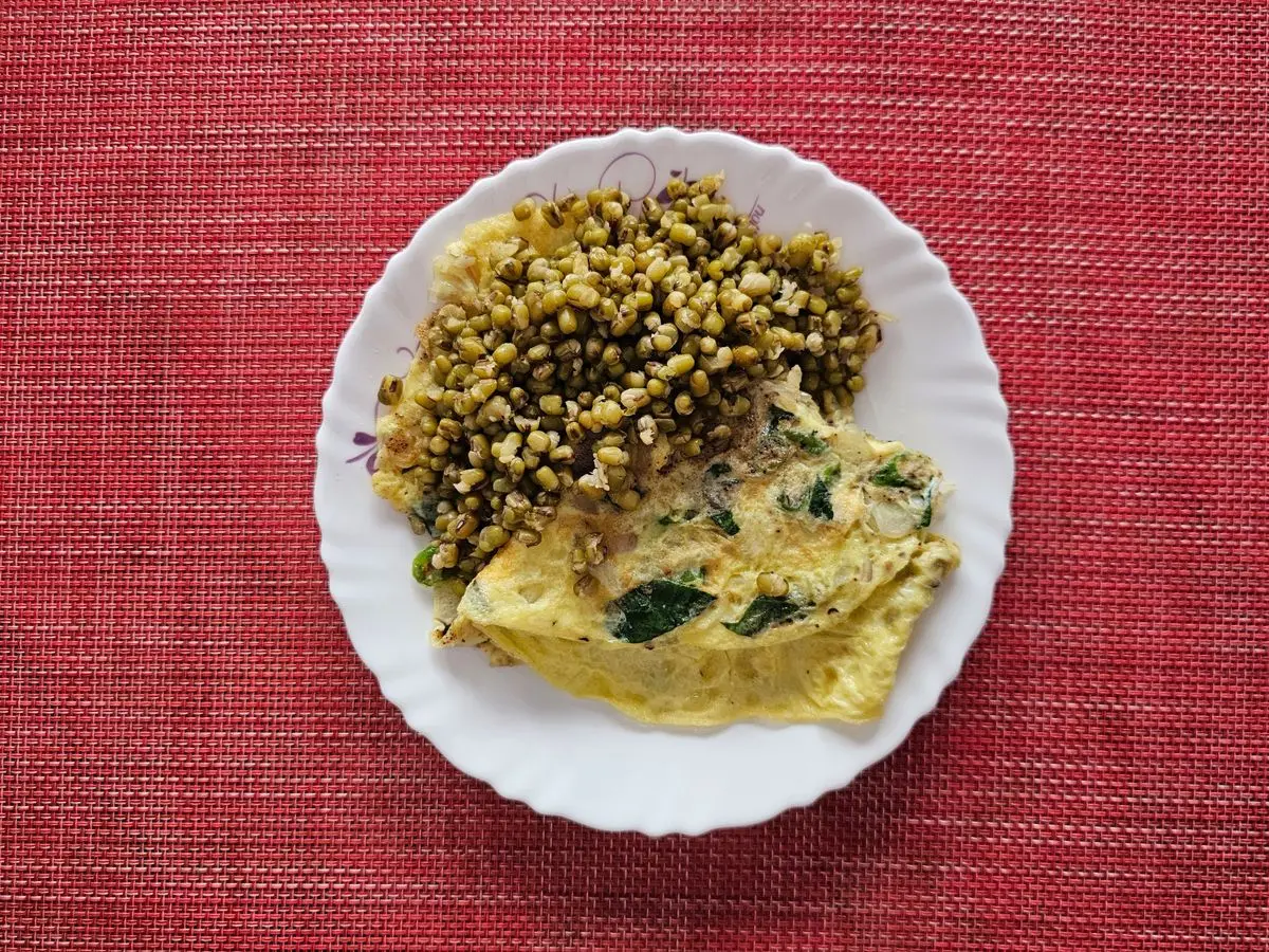 Tortilla francesa con hojas verdes junto a un montón de judías mungo en un plato blanco
