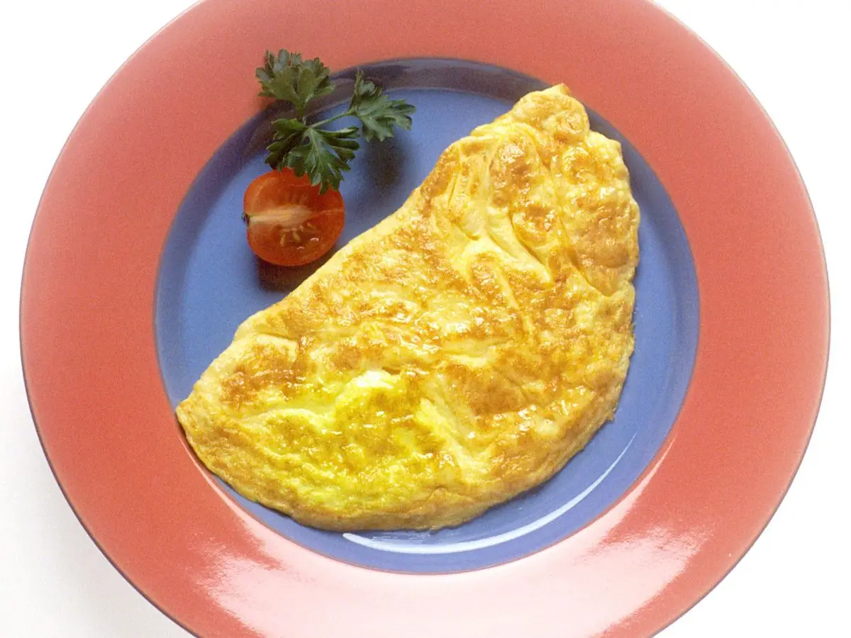 Tortilla francesa doblada en un plato con tomatito cherry y una ramita de perejil