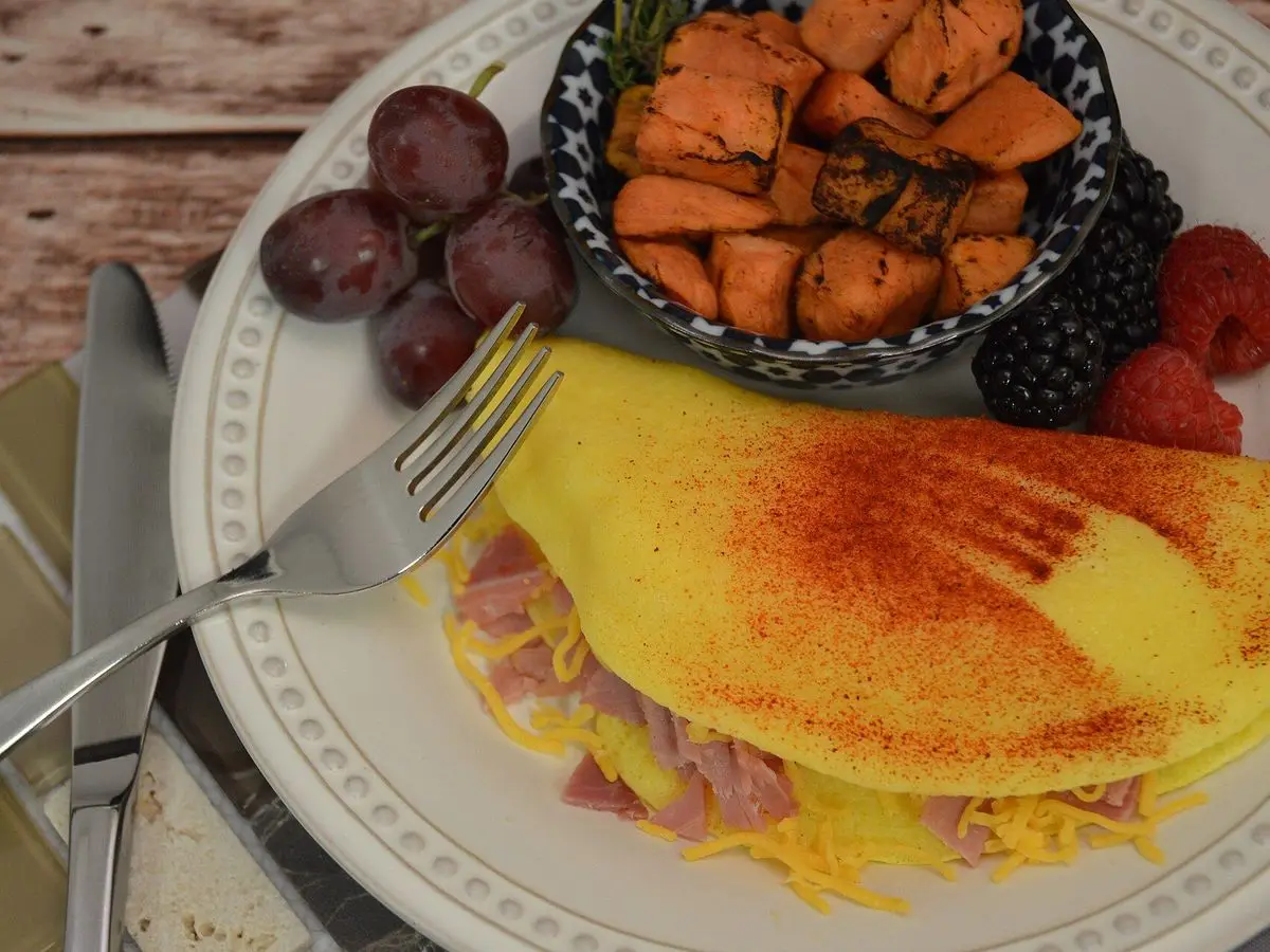 Tortilla doblada rellena de jamón y queso con pimentón en un plato, con boniato asado y uvas al lado