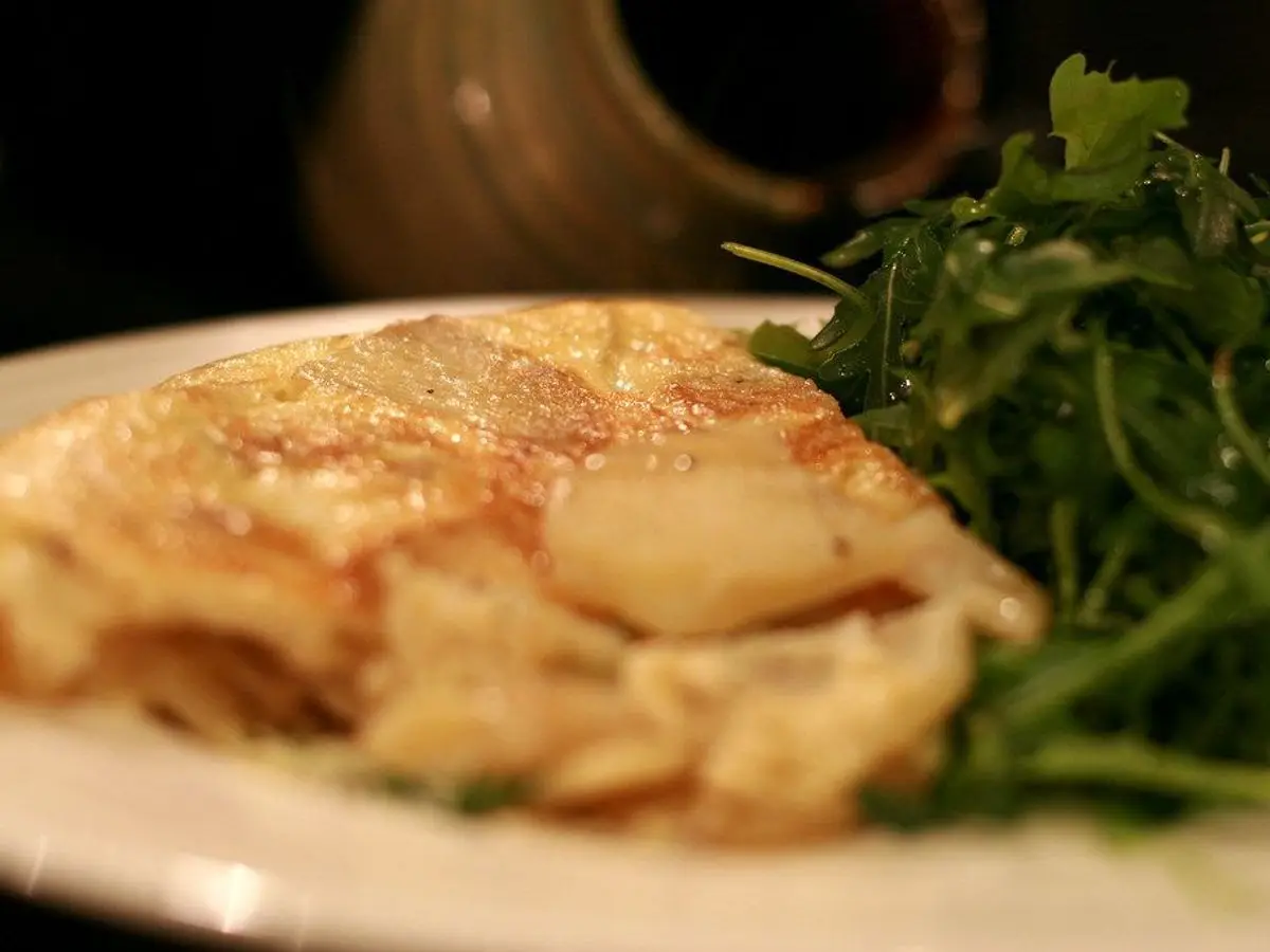 Porción de tortilla de huevo y patata en un plato blanco con ensalada de rúcula al lado