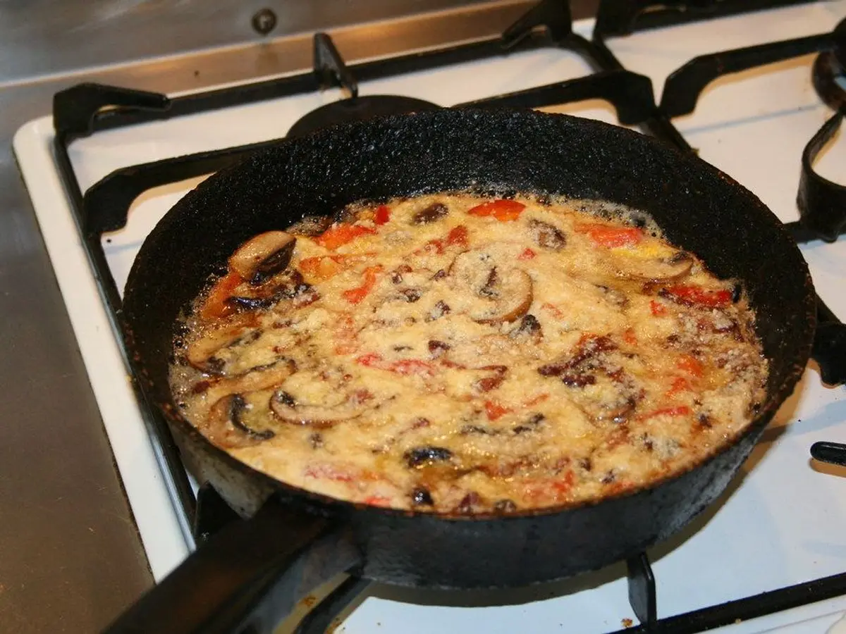 Tortilla en sartén de hierro con setas, pimiento y verduras sobre los fogones