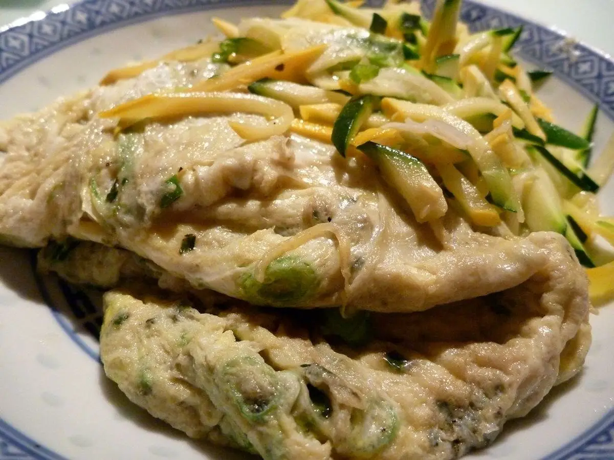 Tortilla doblada con tiras de calabacín y hierbas en un plato con borde azul