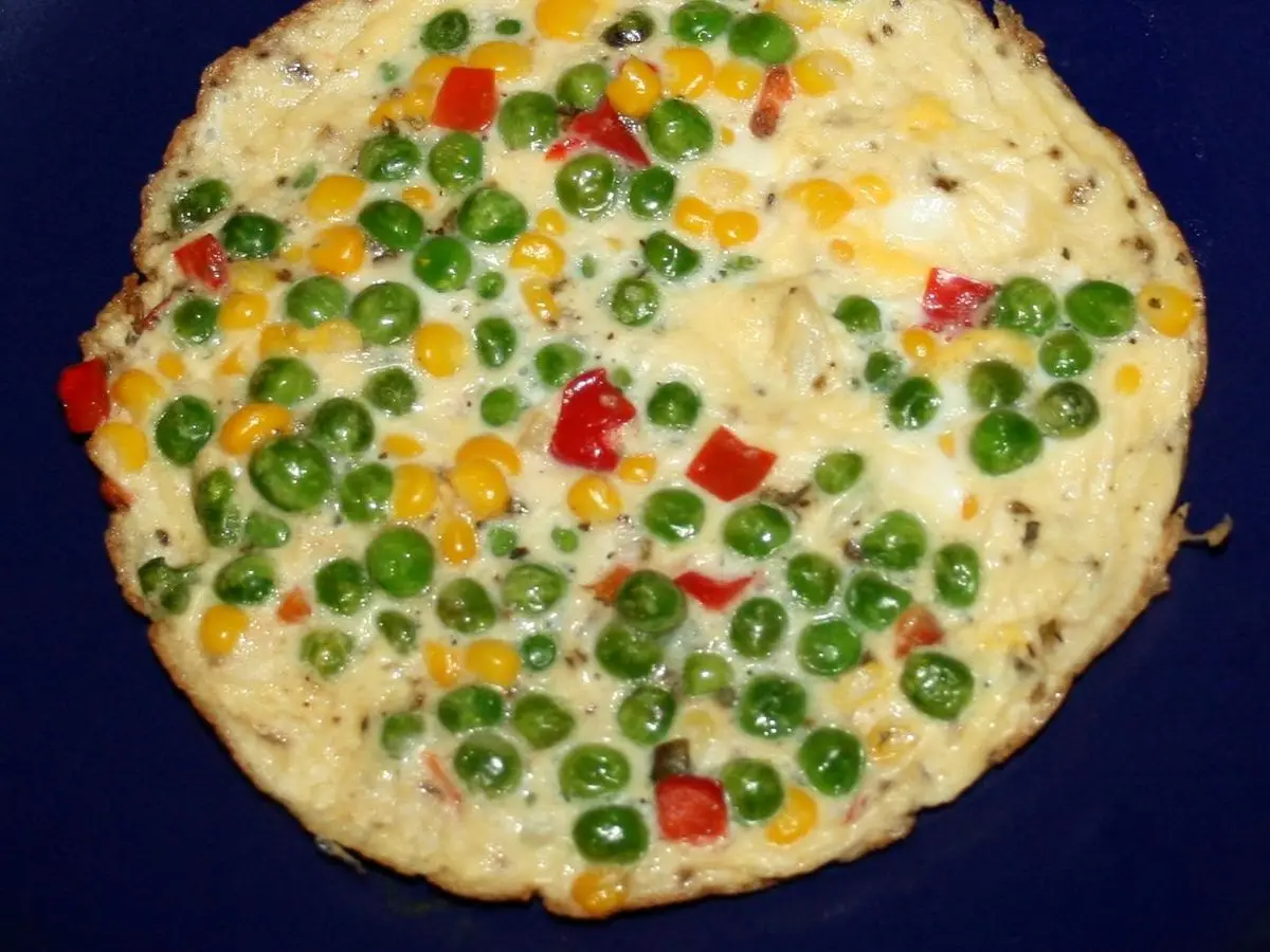 Tortilla redonda de huevo con guisantes, maíz y pimiento rojo sobre un plato azul