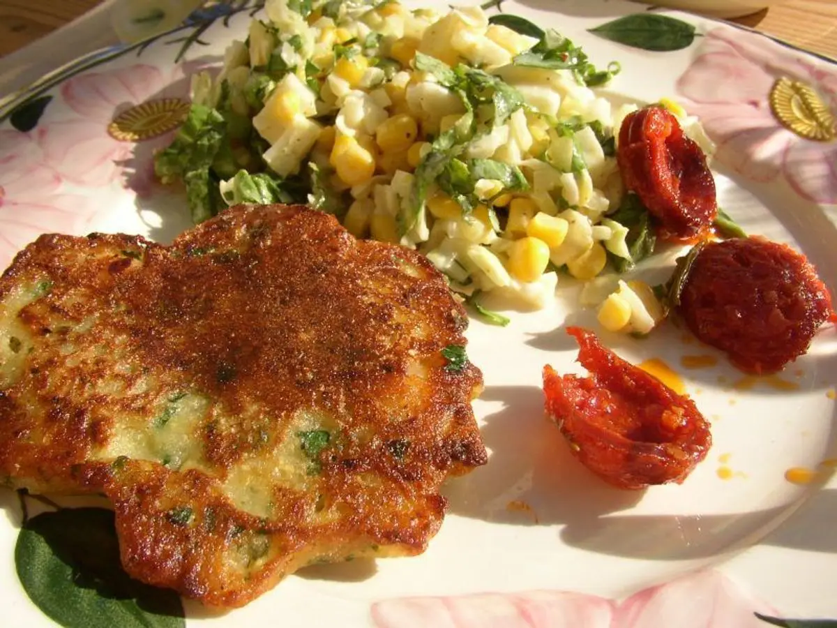 Tortillita de camarones dorada junto a una ensalada de maíz y lechuga con tomates secos en un plato floreado