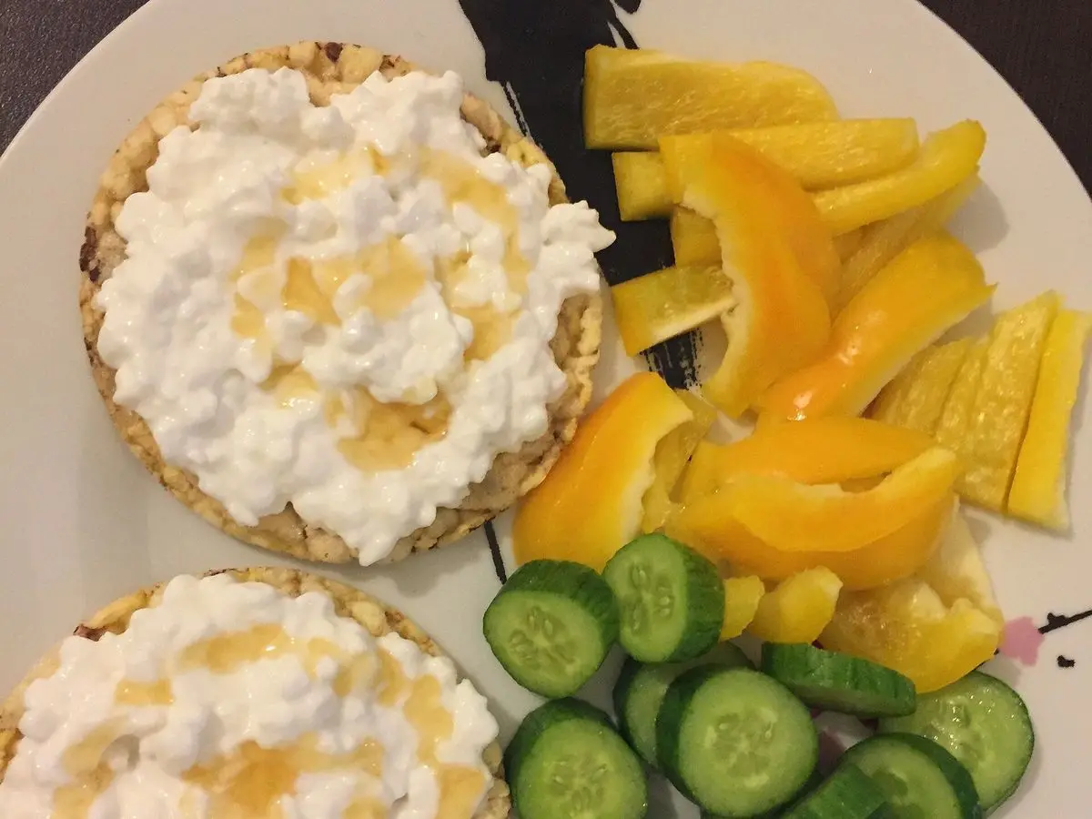 Dos tortitas de arroz con requesón junto a pimiento amarillo y rodajas de pepino en un plato