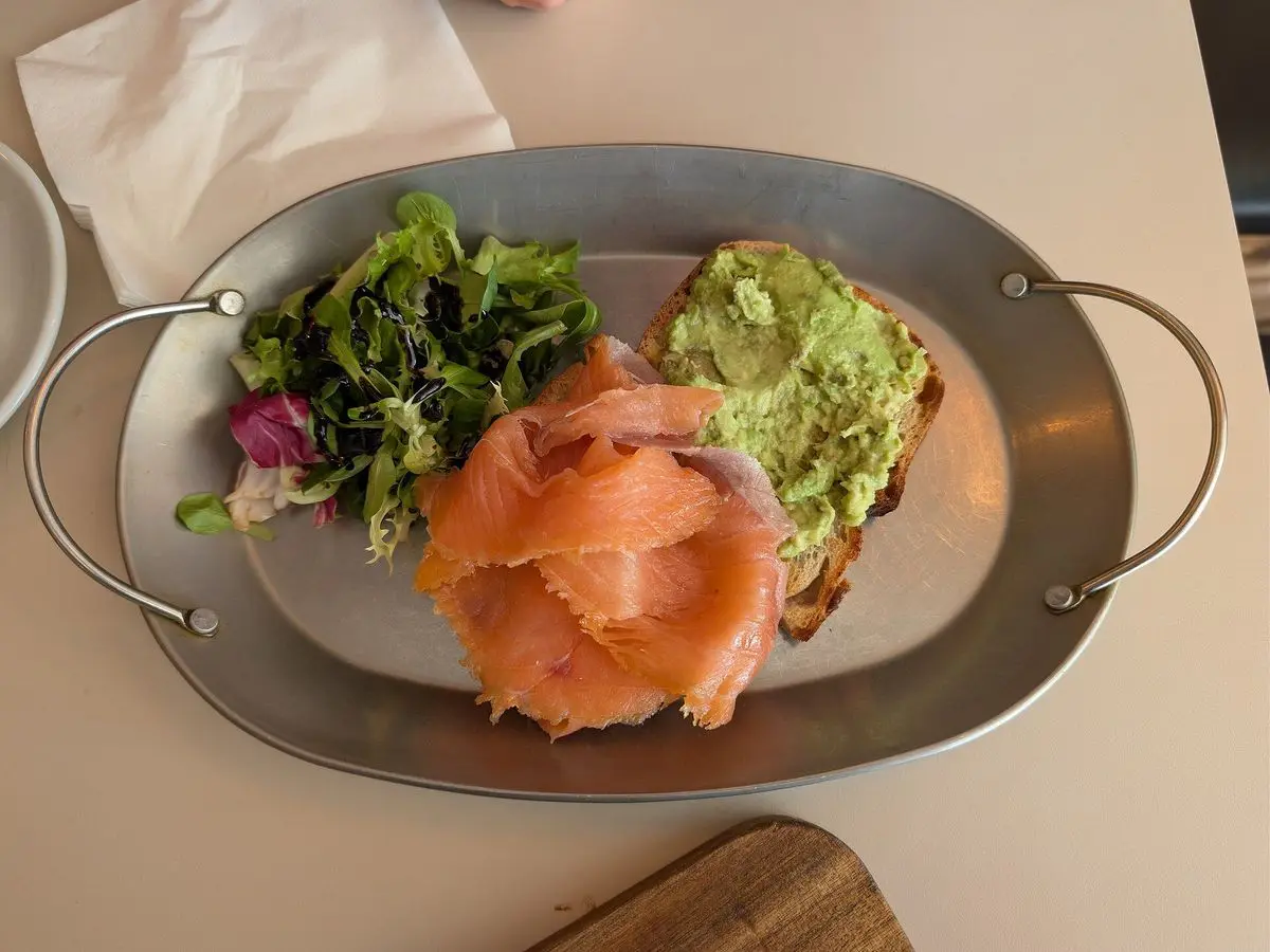 Tostadas con salmón ahumado, aguacate y hojas verdes servidas en una bandeja metálica