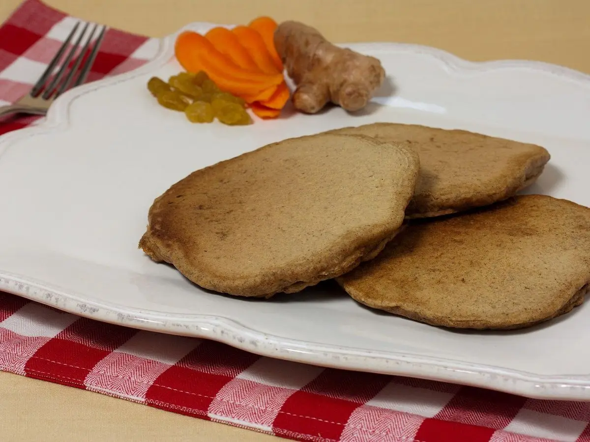 Tres tortitas de zanahoria con jengibre y pasas en un plato blanco con zanahoria laminada