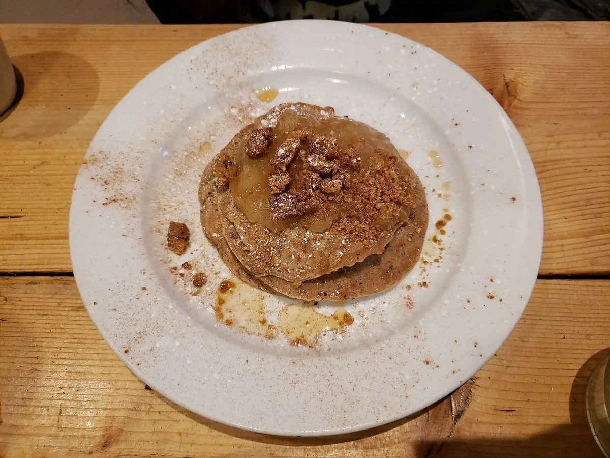 Tortita con canela y frutos secos sobre un plato blanco en una mesa de madera