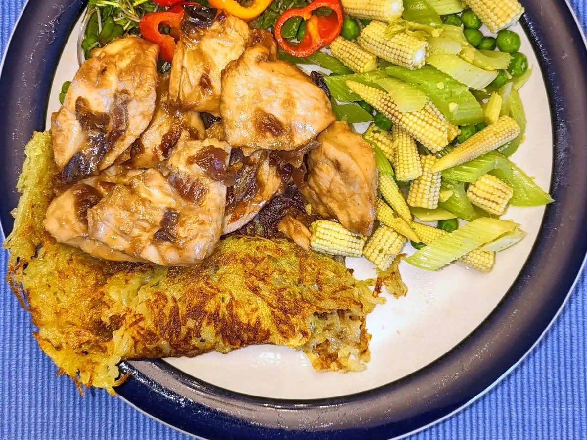 Trozos de pollo con mazorquitas de maíz, pimiento y una tortita dorada en un plato