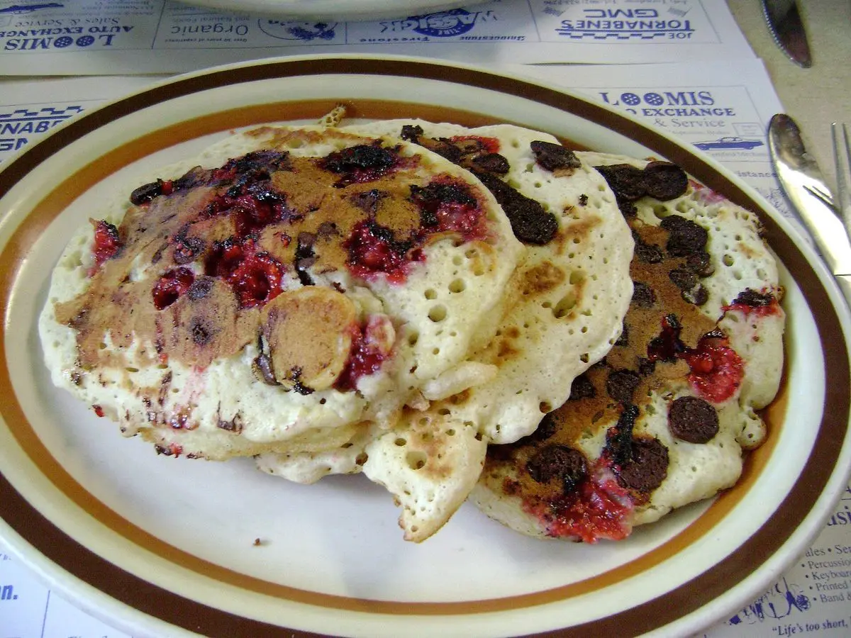 Tortitas con frambuesas y trozos de chocolate sobre un plato con borde dorado