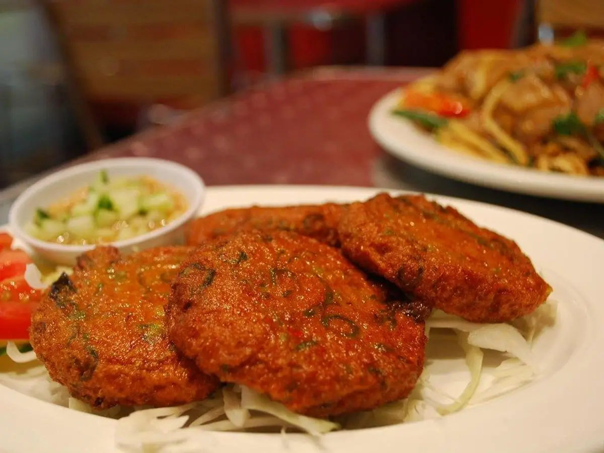 Tortitas fritas de pescado al estilo tailandés con ensalada de pepino y salsa sobre un plato blanco