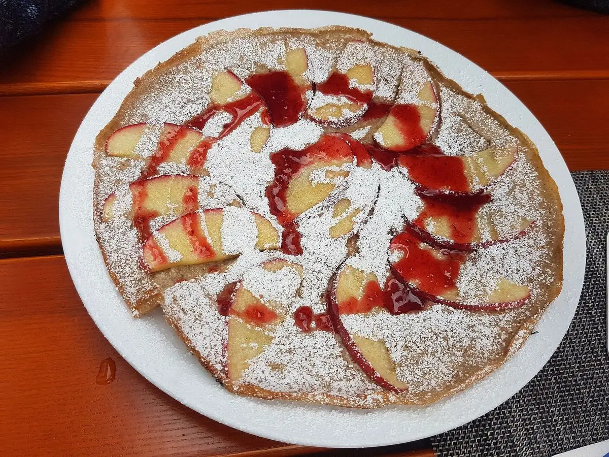 Crepe de trigo sarraceno con gajos de manzana, canela, salsa roja y azúcar glas en un plato
