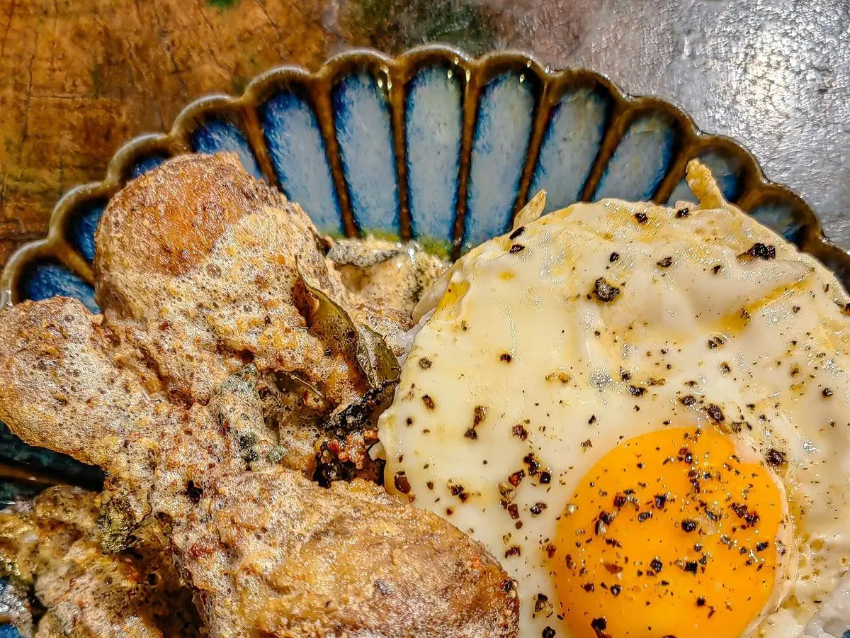 Carne frita dorada con un huevo frito de yema naranja y arroz blanco sobre un plato decorado