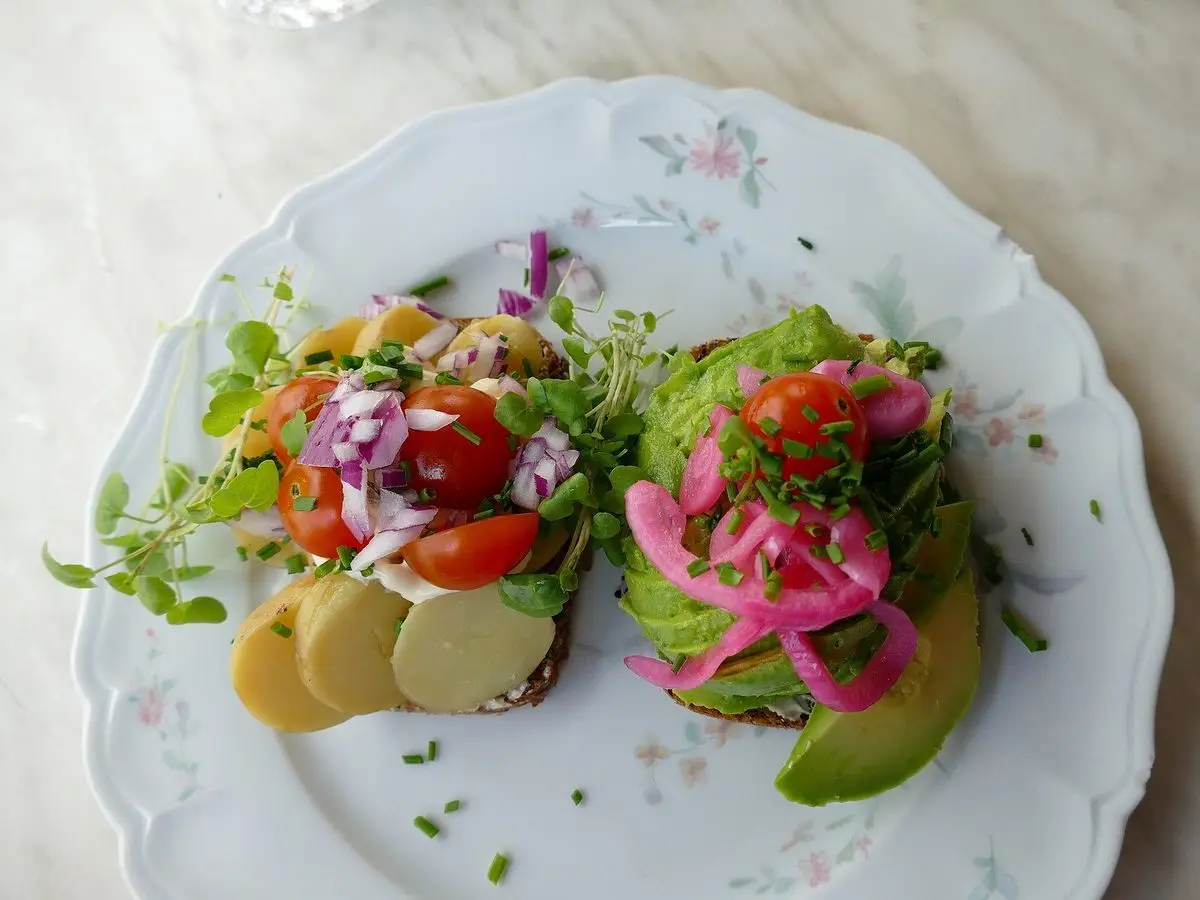Dos tostadas nórdicas con verduras frescas, rodajas de patata y cebolla morada en un plato de porcelana