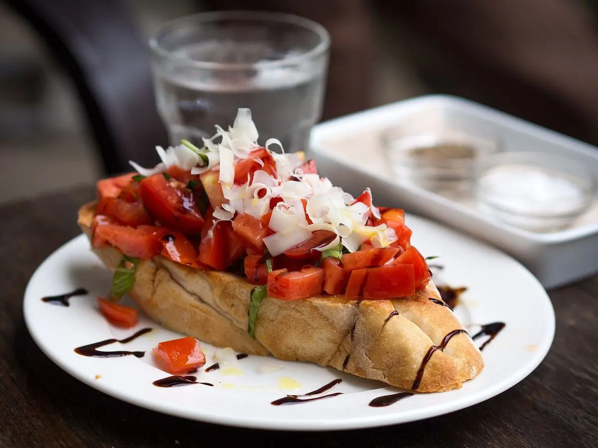 Tosta de pan con tomate troceado y queso blanco rallado con un hilo de balsámico sobre un plato blanco