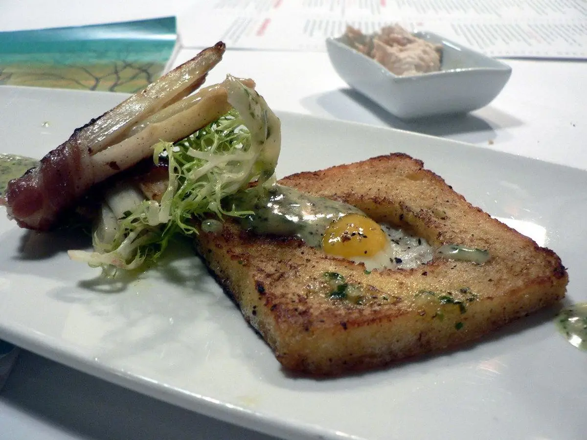 Tostada de pan frito con un huevo de codorniz en el centro y ensalada de escarola en un plato blanco