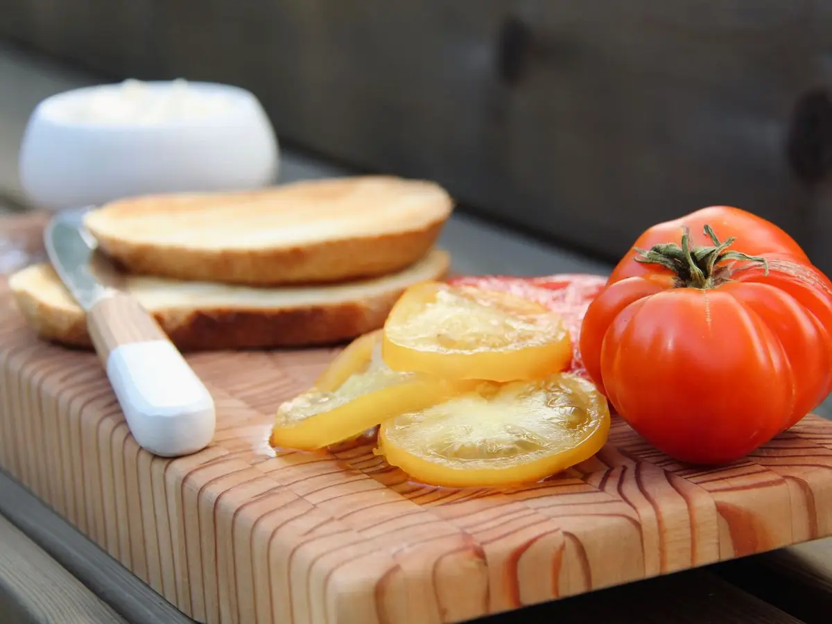 Rebanadas de pan tostado, rodajas de tomate, un tomate entero y embutido sobre una tabla de madera