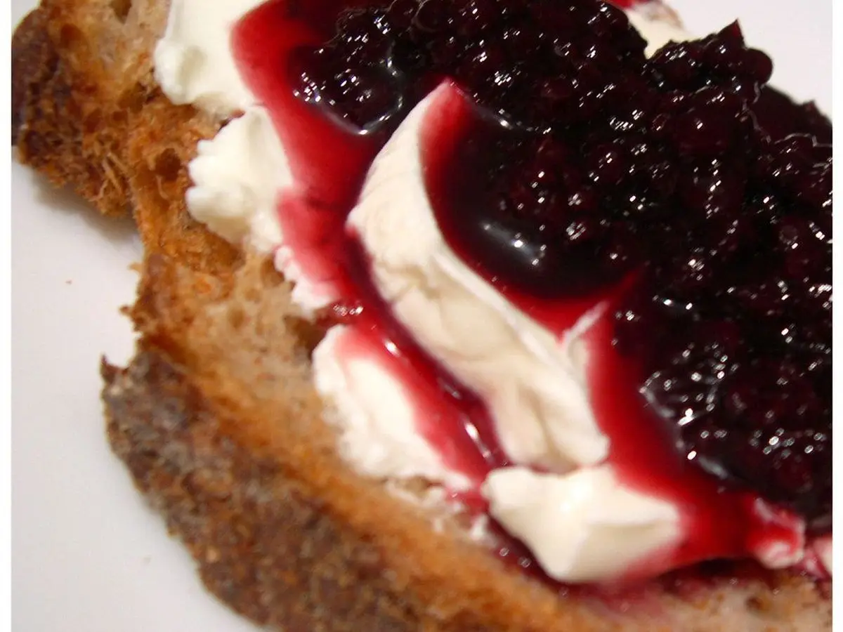 Rebanada de pan integral con queso fresco cremoso y mermelada de frutos rojos