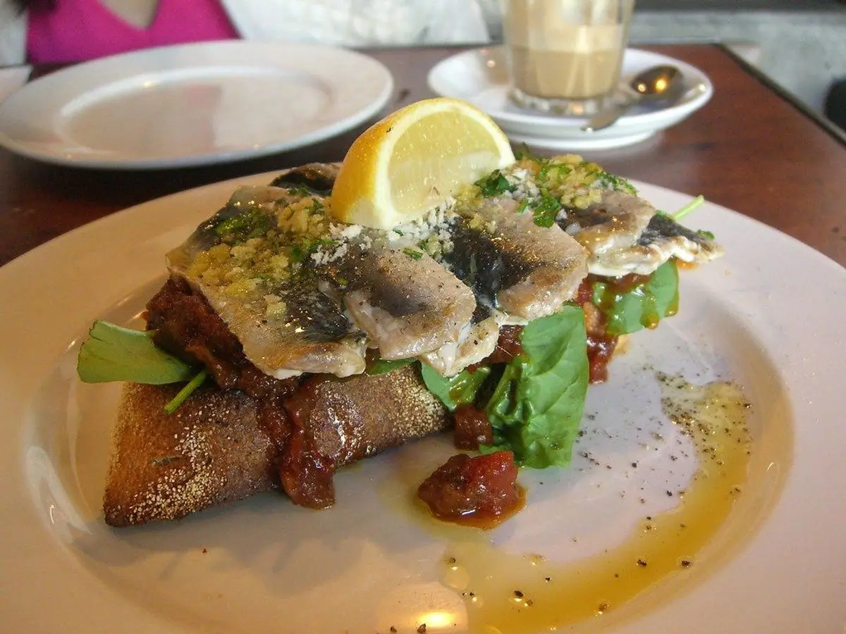 Tostada de pan con sardinas, limón y hierbas sobre un plato blanco