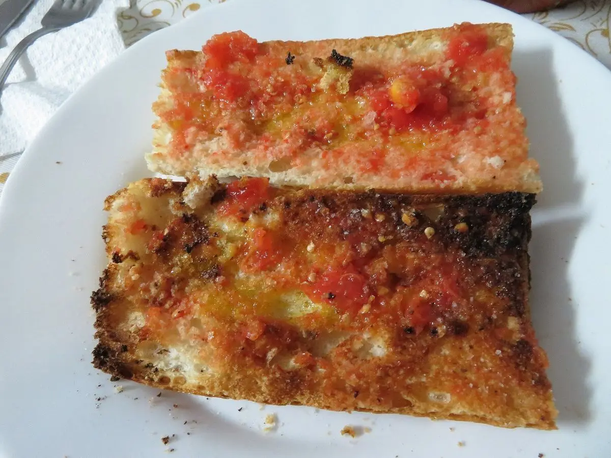 Dos rebanadas de pan tostado cubiertas de tomate rallado y aceite sobre un plato blanco