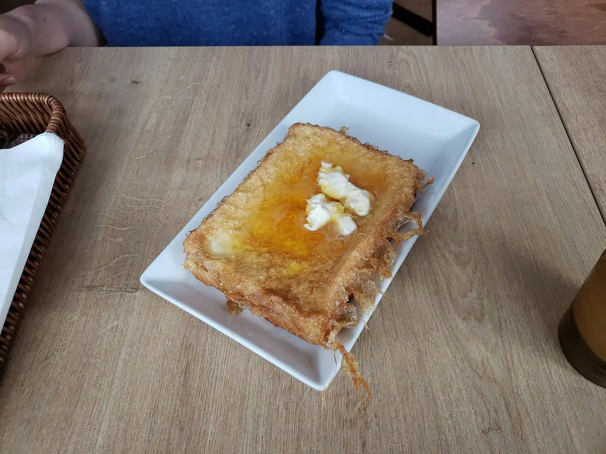 Tostada francesa dorada con mantequilla y almíbar sobre un plato blanco cuadrado