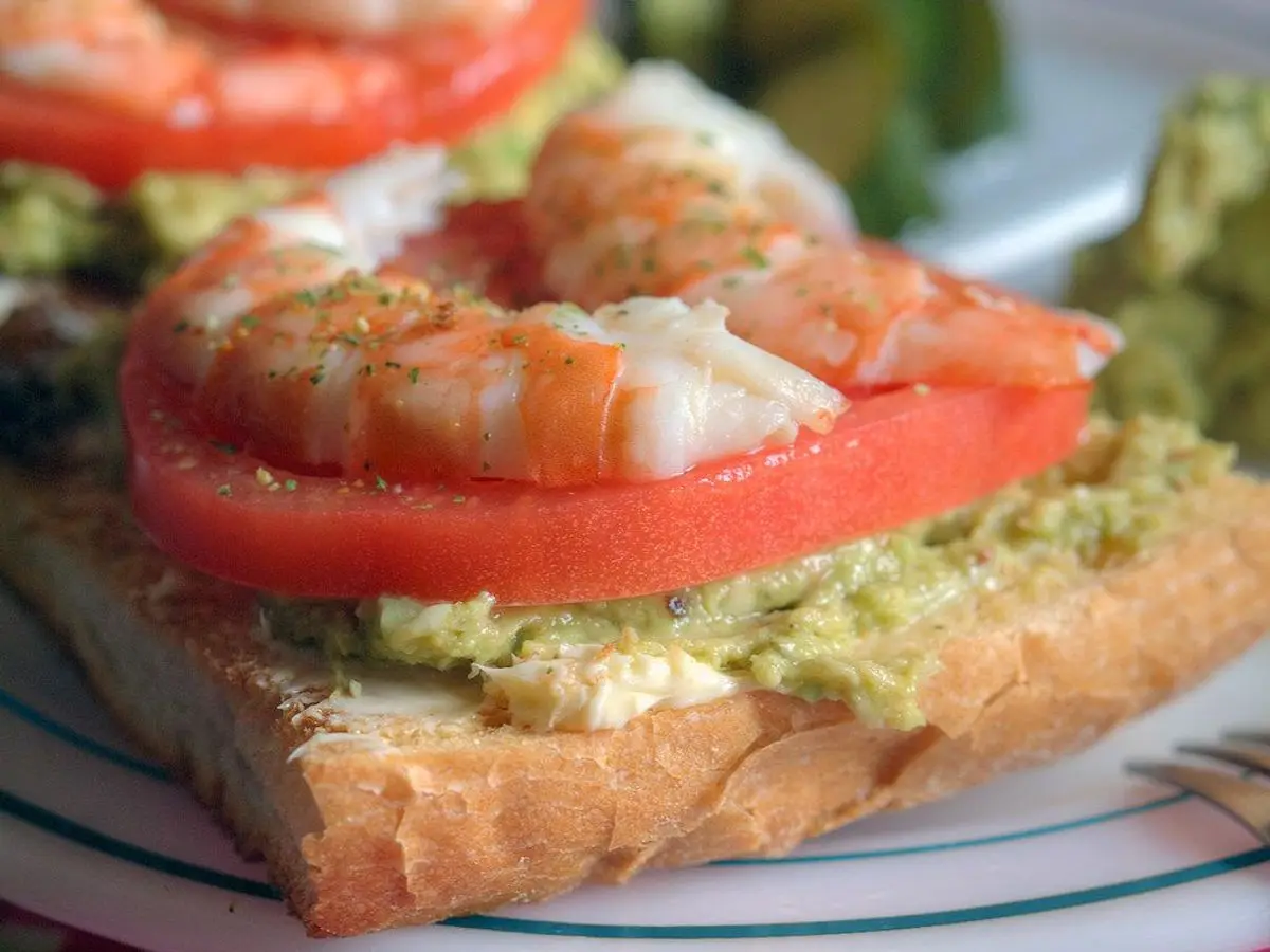 Tostada de pan con aguacate aplastado, gambas y rodajas de tomate