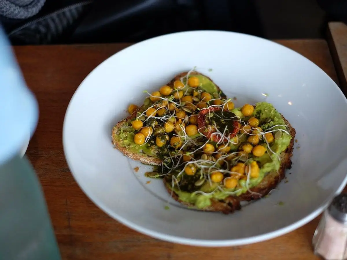Plato blanco con tostada de aguacate cubierta de garbanzos especiados y brotes