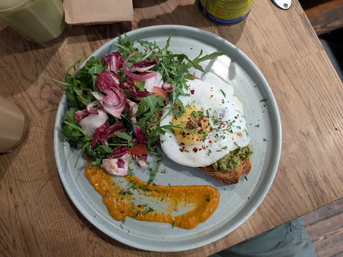 Tostada con huevo escalfado, rúcula y rábano sobre salsa naranja en un plato gris