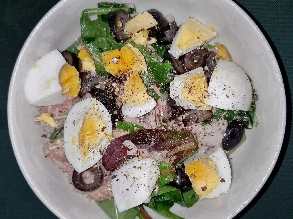 Plato hondo de ensalada con atún, huevo duro en cuartos, aceitunas negras y hojas verdes