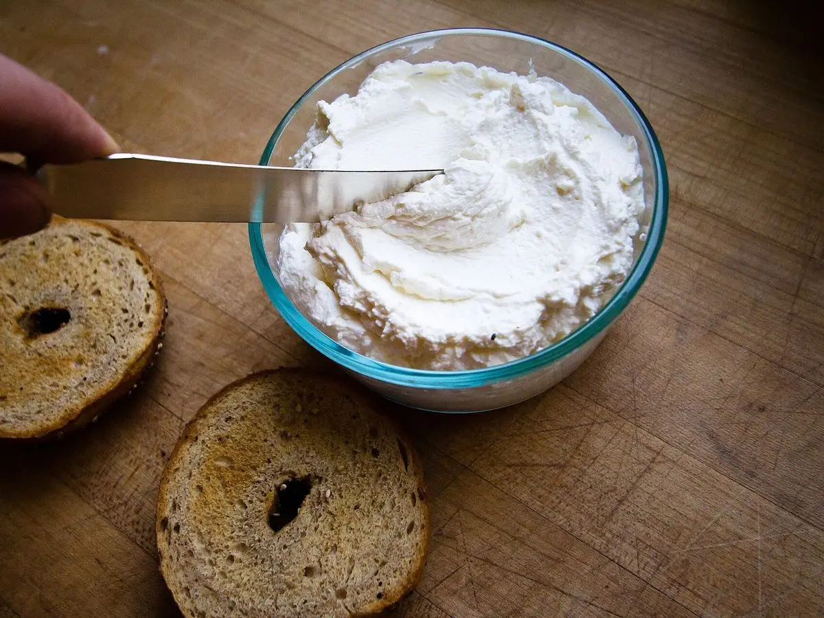 Mitades de pan de bagel junto a un cuenco de queso crema para untar