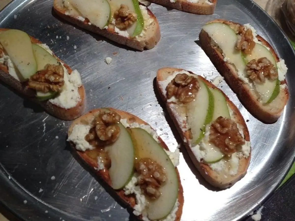 Tostaditas de pan con requesón, láminas de pera, nueces y miel en una bandeja metálica