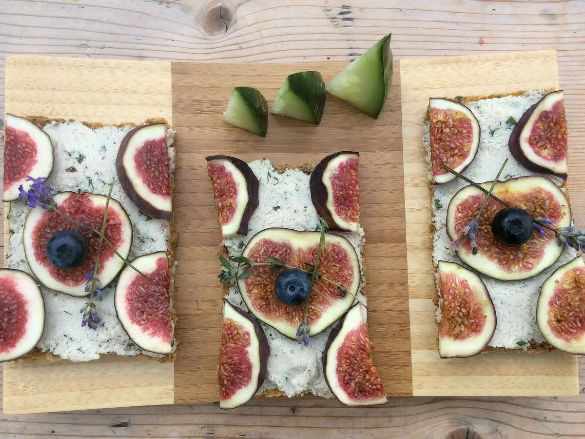 Tostadas rectangulares con crema de queso, rodajas de higo y arándanos sobre una tabla de madera
