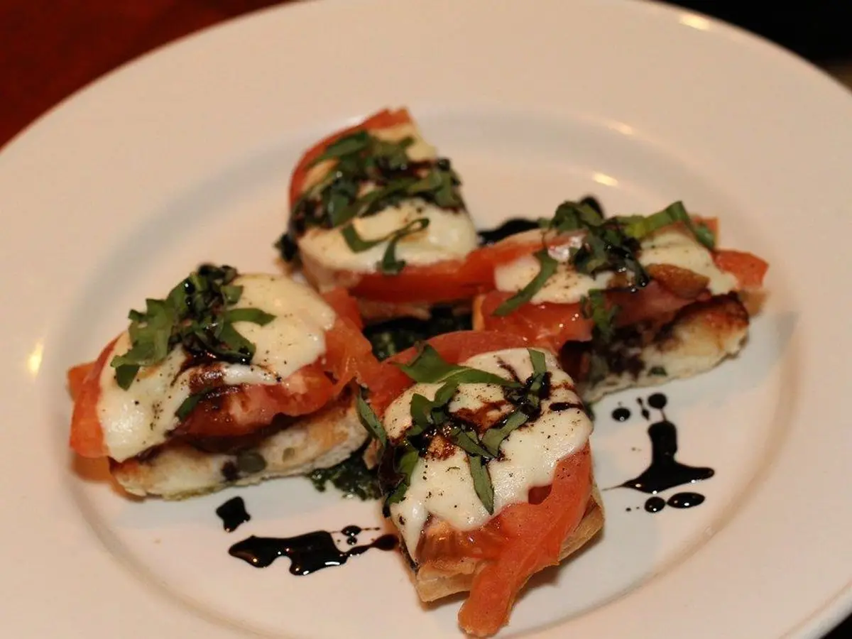 Tostadas con queso fresco blanco, rodajas de tomate y hojas de albahaca sobre un plato blanco